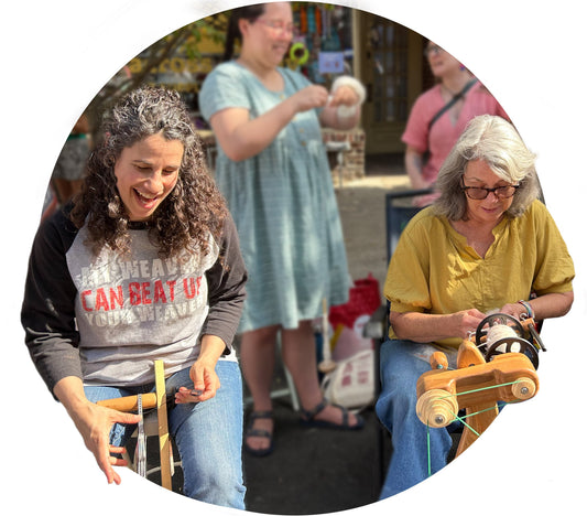 Two women laughing and spinning yarn at a festival